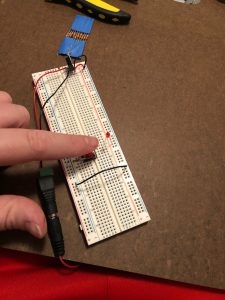 Breadboard with tactile button switch, voltage regulator, 220mA resistor, and ~2V LED.